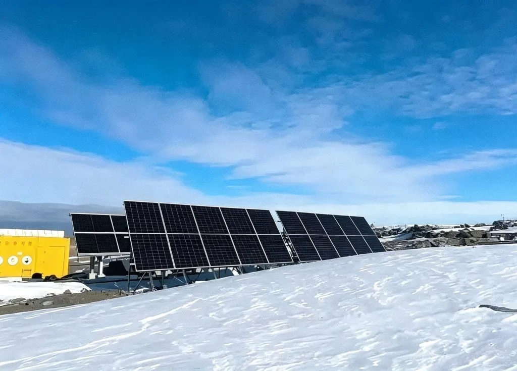 Snow-covered ground in front of a ground-mounted solar array with a yellow equipment container at a remote Canadian ranch