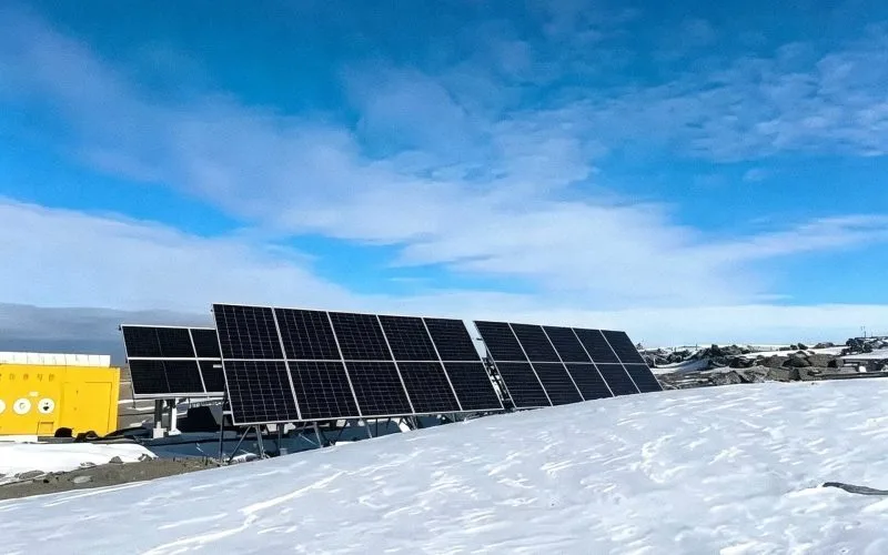 Snow-covered ground in front of a ground-mounted solar array with a yellow equipment container at a remote Canadian ranch