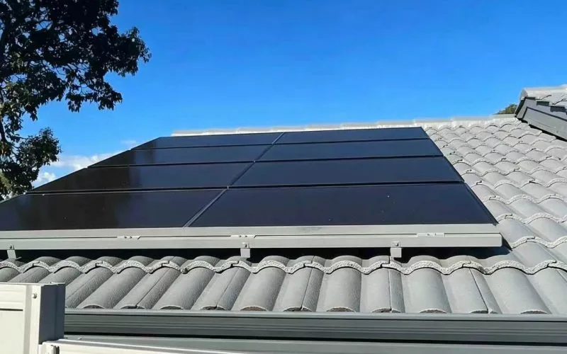 Flush-mounted black solar panels on the tiled roof of a Brazilian house under a clear blue sky